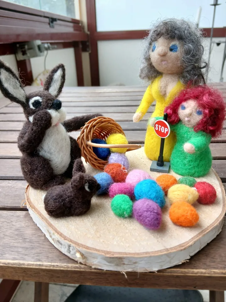 Frühlingsszene mit zwei Hasen, zwei Filzfiguren und einem Korb voller bunter Filzeier.